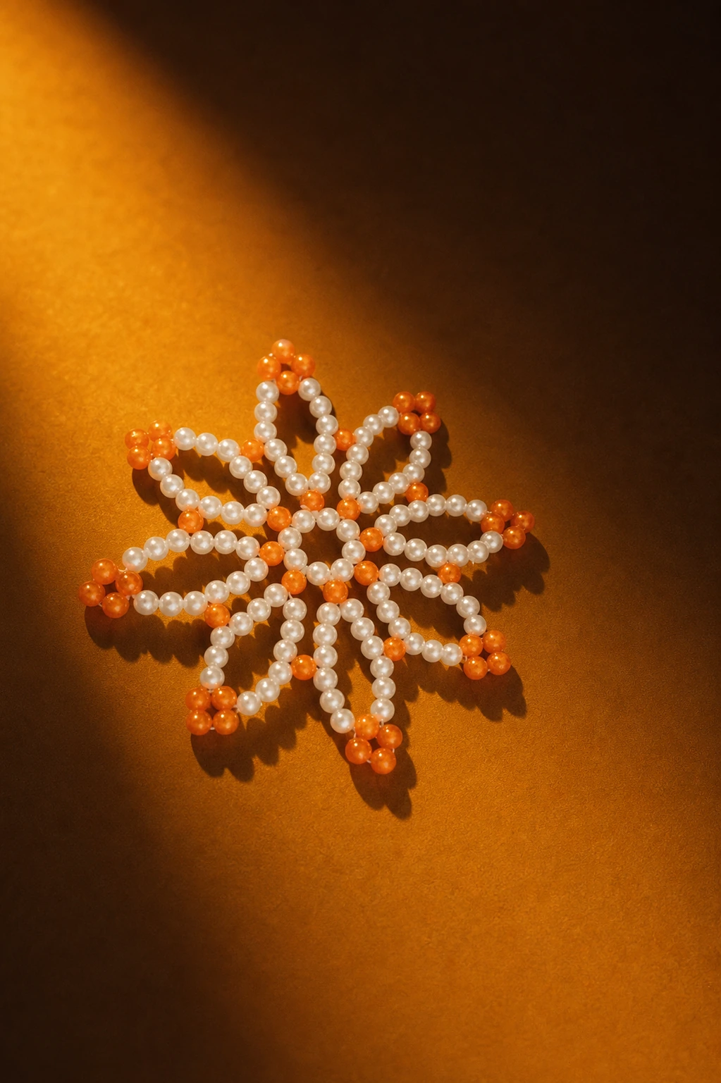 Orange and cream handmade bead flower arranged on a glowing amber surface.