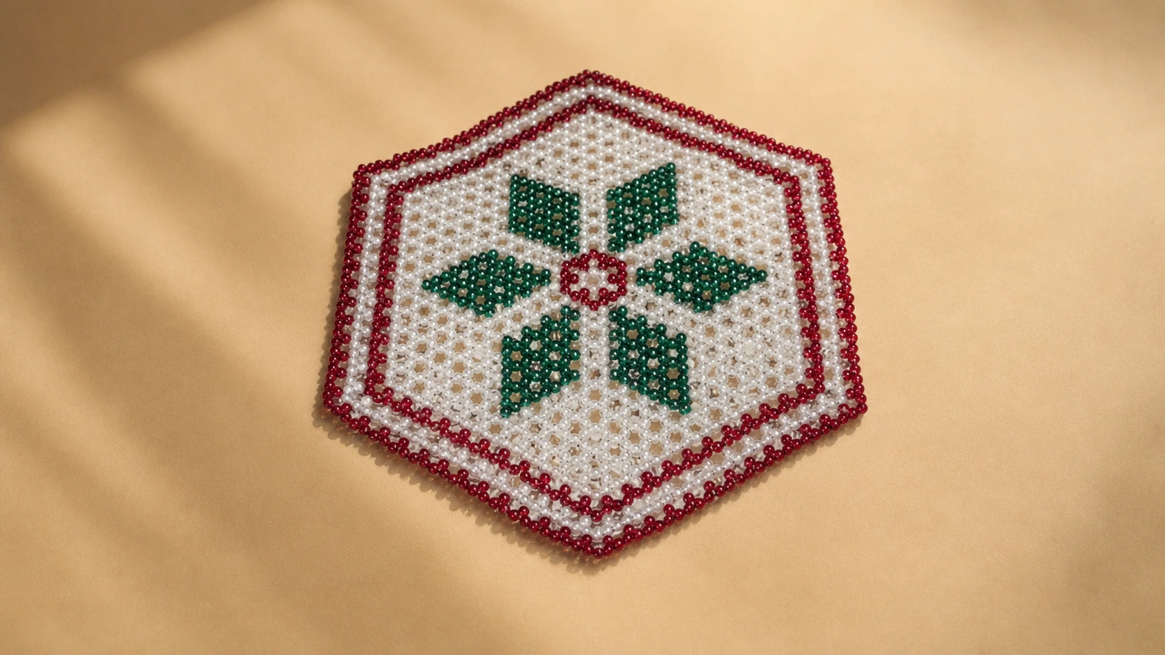Green, red, and cream handmade bead rangoli on a cream surface.
