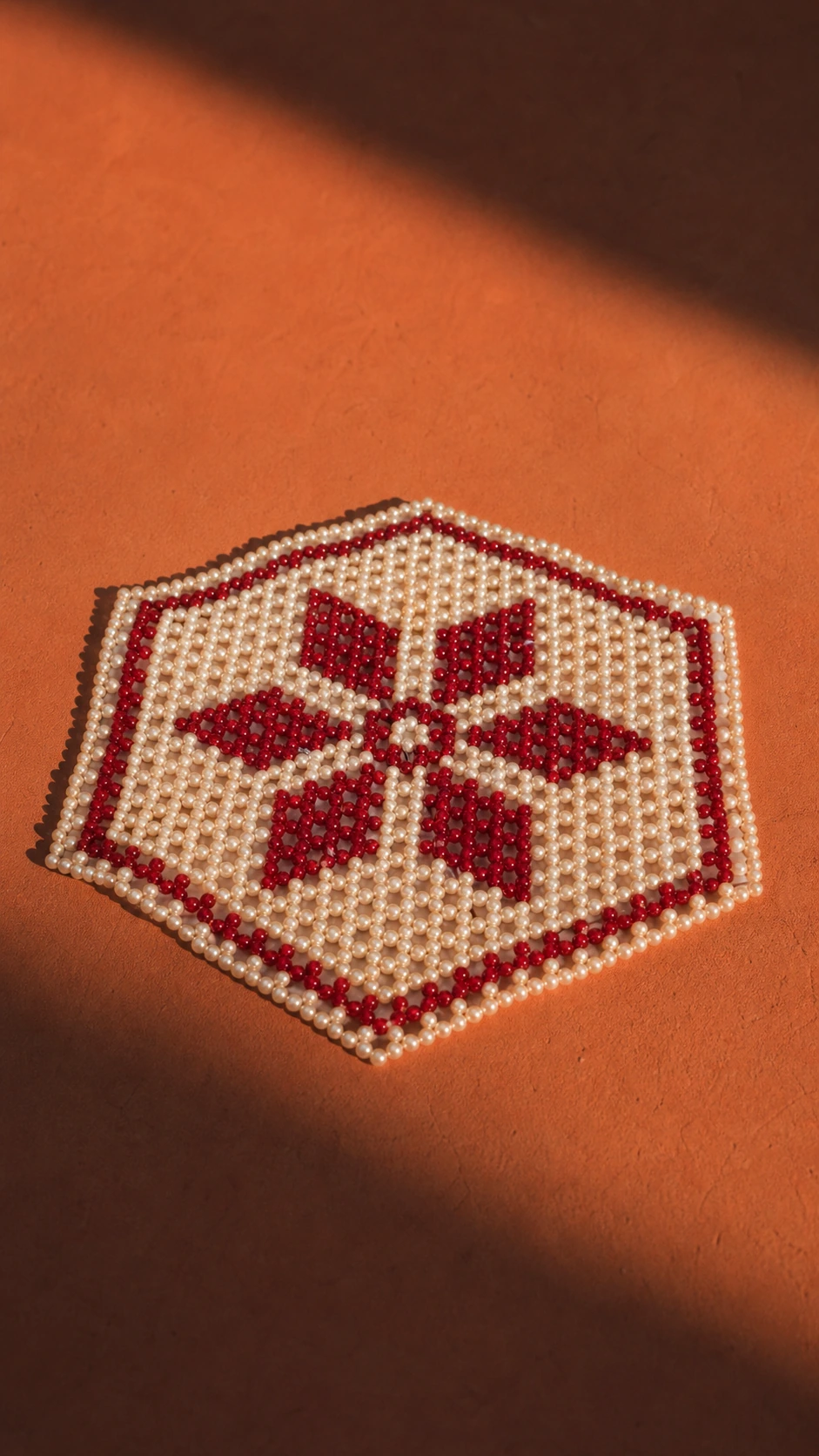 Cream and red handmade bead rangoli on a terracotta surface.