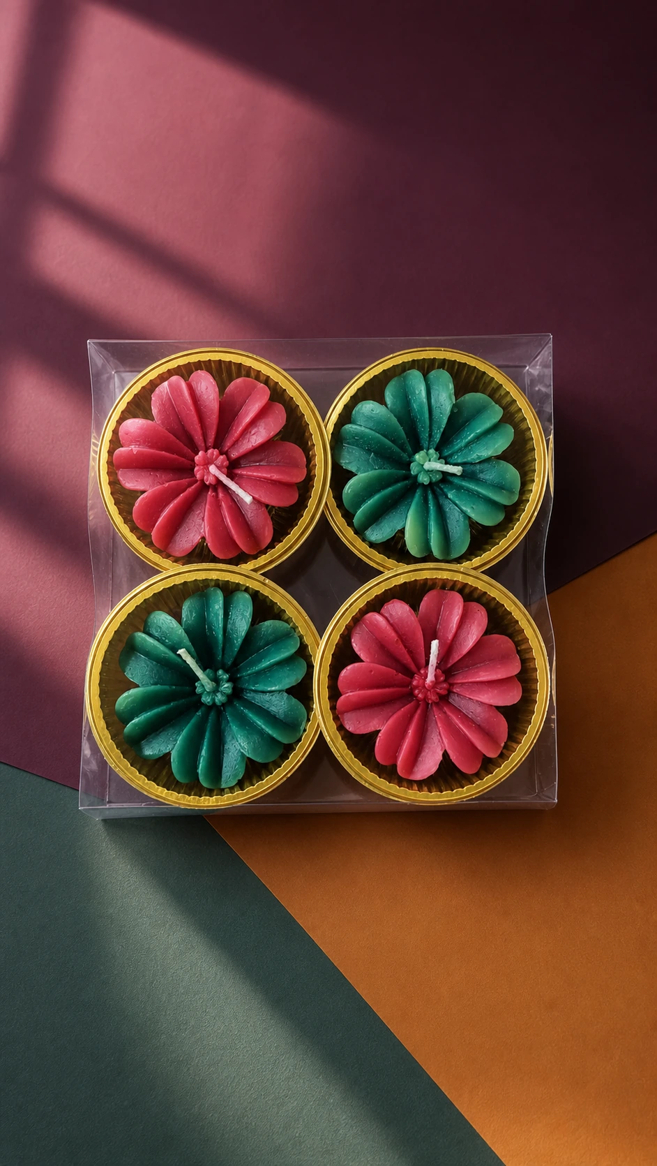 Four pink and teal flower candles in gold cups inside a clear gift box.